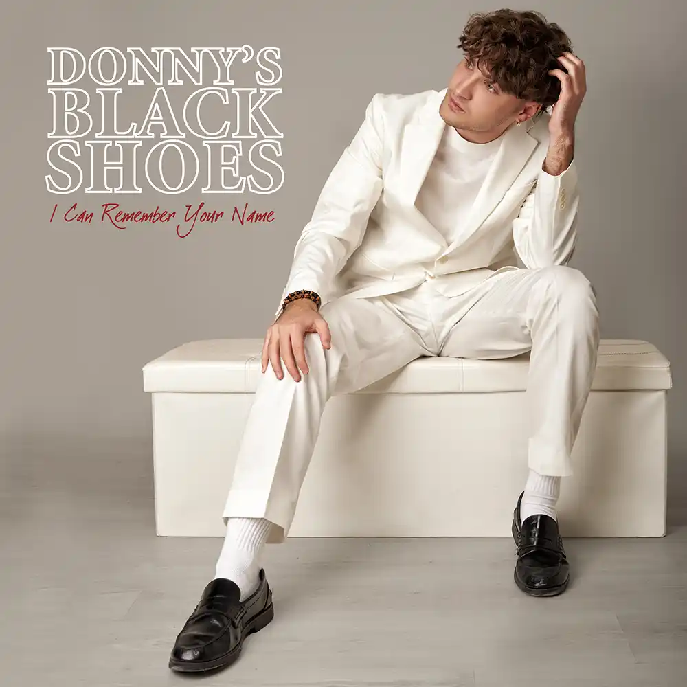 Donny’s Black Shoes vestido con traje blanco sentado sobre un mueble blanco y fondo gris claro Donny’s Black Shoes "I Can Remember Your Name"