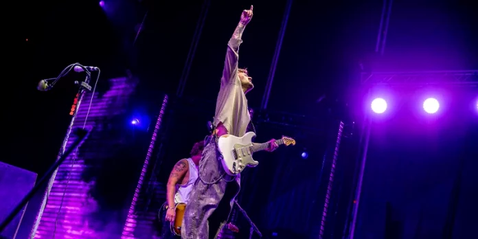 Dani Fernández levantando la mano con su guitarra blanca bajo luces moradas en concierto