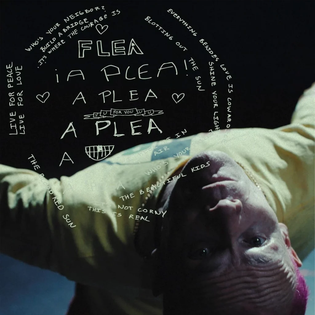 Primer plano invertido de Flea (con cabello rosa) del videoclip A Plea, con el título de la canción y letras manuscritas en blanco sobre el fondo oscuro. Flea A Plea nuevo álbum 2026