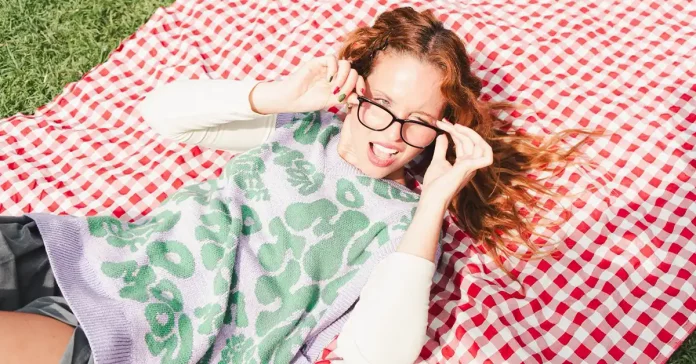 Persona joven pelirroja con gafas posando en una manta de picnic